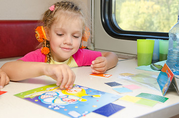 Image showing A small child in a train of fun playing at the table at the lower place in the second-class compartment wagon