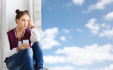 Image showing teenage girl sitting on windowsill with smartphone