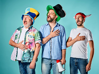 Image showing The three football fans singing the national anthem over blue