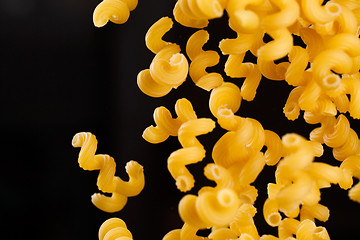 Image showing Falling cavatappi pasta. Flying yellow raw macaroni over black background. 