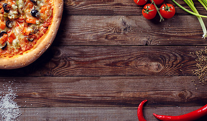 Image showing Italian pizza with tomatoes on a wooden table, top view.