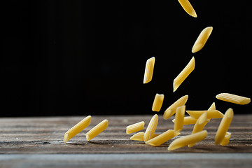 Image showing Falling penne pasta. Flying yellow raw macaroni over black background.