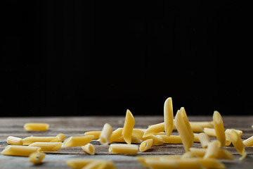 Image showing Falling penne pasta. Flying yellow raw macaroni over black background.