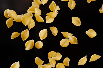 Image showing Falling conchiglie pasta. Flying yellow raw macaroni over black background.