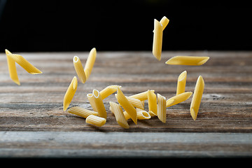 Image showing Falling penne pasta. Flying yellow raw macaroni over black background.