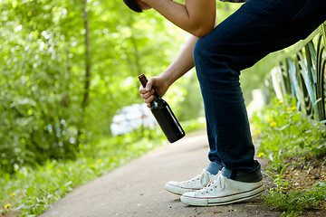 Image showing Man depressed with beer bottle sitting on green fence outdoor. 