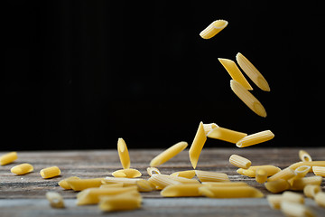 Image showing Falling penne pasta. Flying yellow raw macaroni over black background.