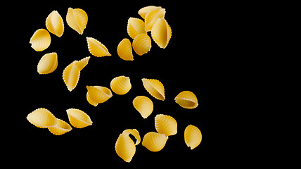 Image showing Falling conchiglie pasta. Flying yellow raw macaroni over black background.