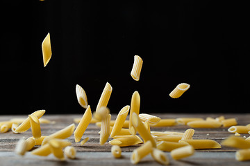 Image showing Falling penne pasta. Flying yellow raw macaroni over black background.