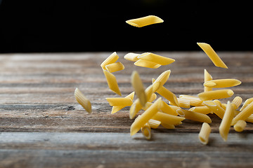 Image showing Falling penne pasta. Flying yellow raw macaroni over black background.