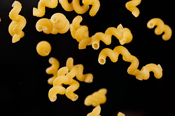 Image showing Falling cavatappi pasta. Flying yellow raw macaroni over black background. 