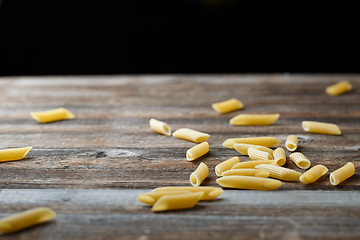 Image showing Falling penne pasta. Flying yellow raw macaroni over black background.