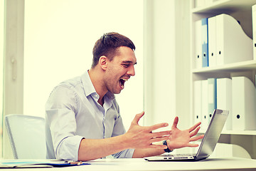 Image showing angry businessman with laptop and papers in office