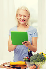 Image showing smiling young woman with tablet pc cooking at home