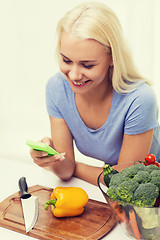 Image showing smiling woman with smartphone cooking vegetables