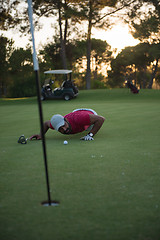 Image showing golf player blowing ball in hole with sunset in background