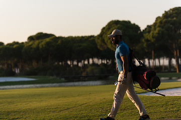 Image showing golfer  walking and carrying golf  bag at beautiful sunset