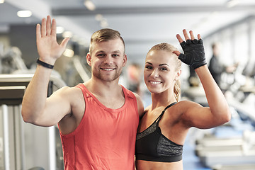 Image showing smiling man and woman waving hands in gym