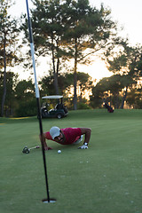 Image showing golf player blowing ball in hole with sunset in background
