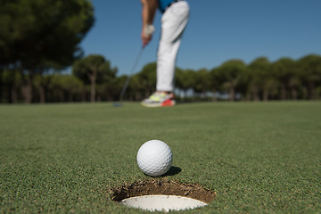 Image showing golf player hitting shot, ball on edge of hole