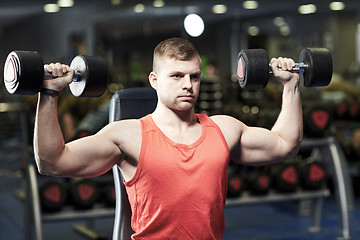 Image showing young man with dumbbells flexing muscles in gym