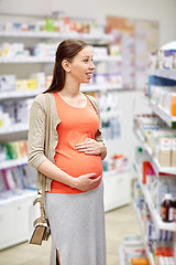 Image showing happy pregnant woman choosing medicine at pharmacy