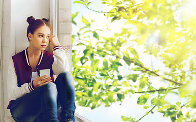 Image showing teenage girl sitting on windowsill with smartphone