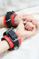 Image showing female hands in leather handcuffs. on the background sheet. sex toys.