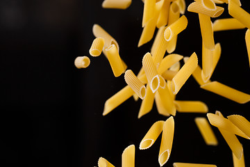 Image showing Falling penne pasta. Flying yellow raw macaroni over black background.