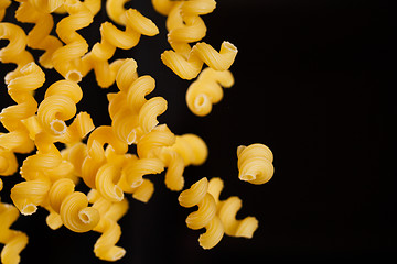 Image showing Falling cavatappi pasta. Flying yellow raw macaroni over black background. 