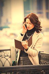 Image showing businesswoman looking in a notebook and talking on mobile phone