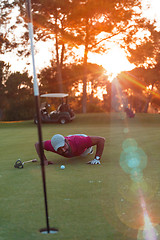 Image showing golf player blowing ball in hole with sunset in background