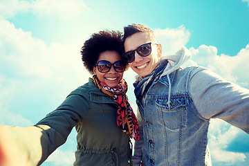 Image showing happy teenage couple taking selfie over blue sky