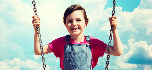 Image showing happy little girl swinging on swing over blue sky