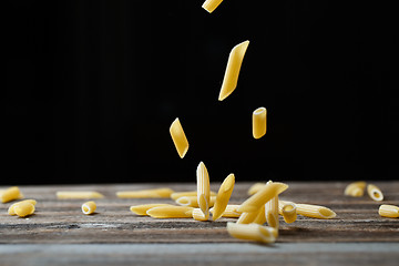 Image showing Falling penne pasta. Flying yellow raw macaroni over black background.