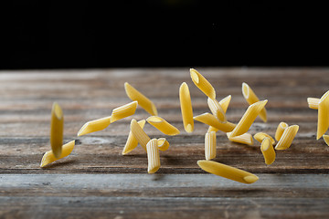 Image showing Falling penne pasta. Flying yellow raw macaroni over black background.