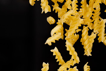 Image showing Falling fusilli pasta. Flying yellow raw macaroni over black background.