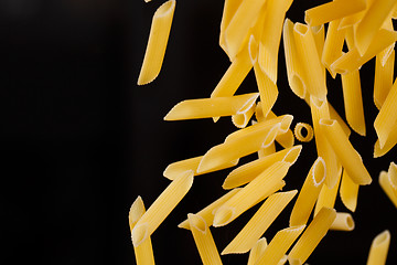 Image showing Falling penne pasta. Flying yellow raw macaroni over black background.