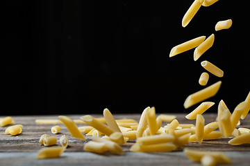 Image showing Falling penne pasta. Flying yellow raw macaroni over black background.