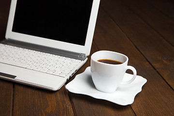 Image showing Fresh black coffee in cup on saucer near laptop