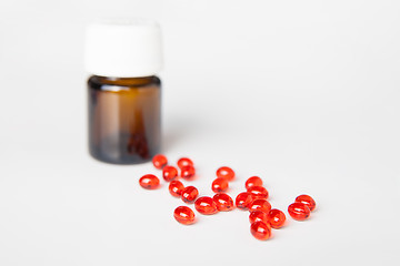 Image showing Pile of red pills on white table. Bottle