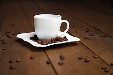 Image showing Aromatic coffee in white cup with saucer and scattered beans