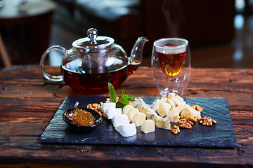 Image showing various cheeses and tea on a wooden background