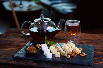 Image showing various cheeses and tea on a wooden background