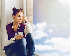 Image showing teenage girl sitting on windowsill with smartphone