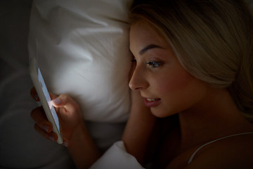 Image showing young woman with smartphone in bed at home bedroom