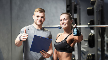 Image showing smiling young woman with personal trainer in gym