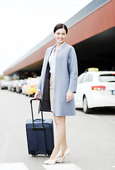 Image showing smiling young woman with travel bag over taxi