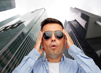 Image showing face of scared man in sunglasses over big city