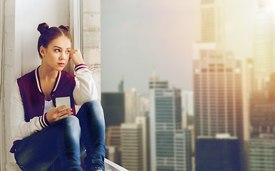 Image showing teenage girl sitting on windowsill with smartphone